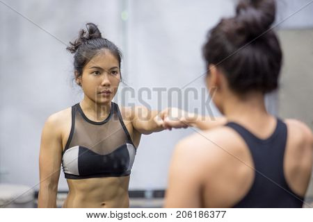 young asian athletic women in sportswear punching and looking herself in the mirror