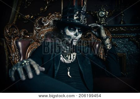 Halloween. A man with a skull makeup dressed in a tail-coat and a top-hat is in the old castle. Baron Saturday. Baron Samedi. Dia de los muertos. Day of The Dead. Old vintage interior.