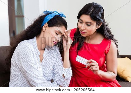 Woman giving to her young female friend medication against severe headache