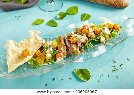 Menu of gastronomic restaurant. Warm salad with chicken baked pumpkin and cheese halumi with fresh herbs on  glass plate on  blue wooden table