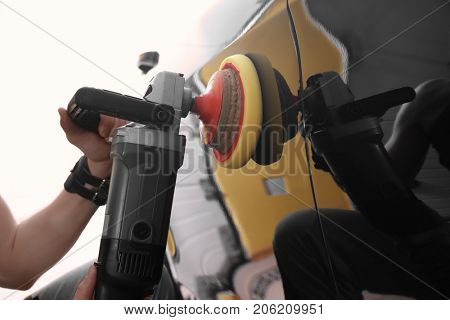 Man polishing car with power buffer machine in repair shop