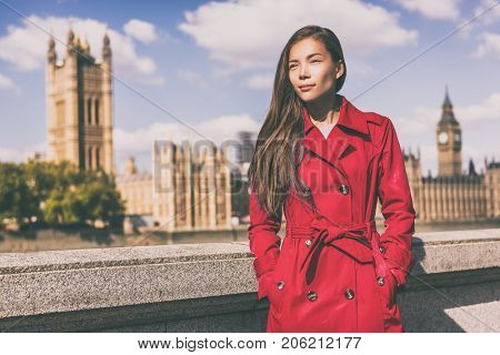 London fashion model in autumn trench coat. Asian woman wearing stylish red fall jacket visiting Westminster and Big Ben, Europe traveler.