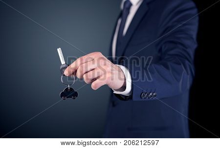 Young businessman hand over keys with empty dark background