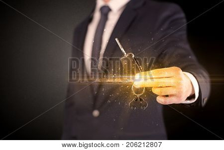 Businessman hand  over shiny keys in dark suit with dark background