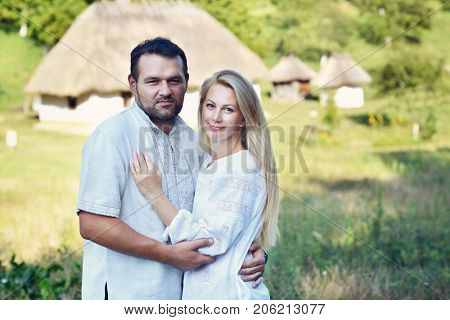 Ukrainian couple in traditional clothing vyshyvanka over landscape of tipical ucrainian village, summer outdoor. Ukrainian people posing near the house, image toned.