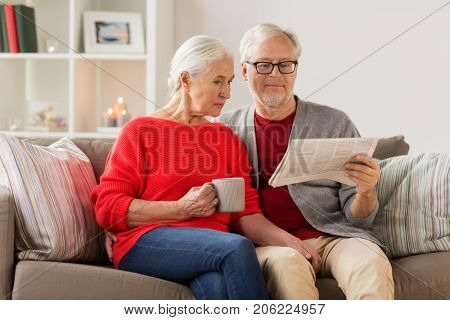 christmas, mass media and people concept - happy senior couple reading newspaper at home