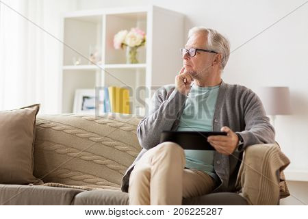 technology, old age, people and lifestyle concept - senior man with tablet pc computer sitting on sofa at home and thinking