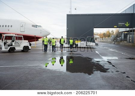 Workers Walking Towards Airplane On Wet Runway