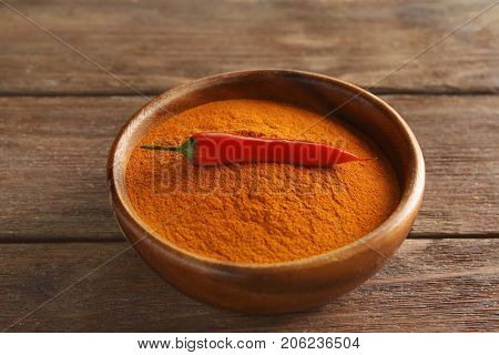 Chili powder and raw pepper in bowl on wooden table