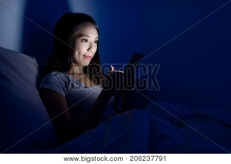 Woman using mobile phone on bed at night
