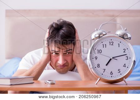 Man in bed frustrated suffering from insomnia with an alarm cloc