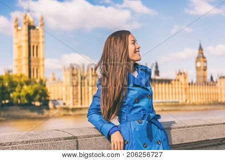London city lifestyle Asian businesswoman Europe autumn travel in blue trench coat. Multiracial model posing in fashion fall outerwear at Westminster and Big Ben, famous european urban destination.