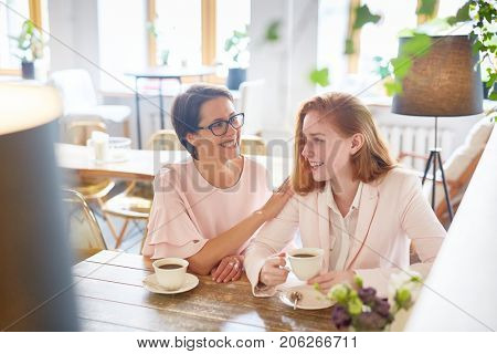 Happy aunt and niece relaxing in cafe and enjoying talk by cup of coffee