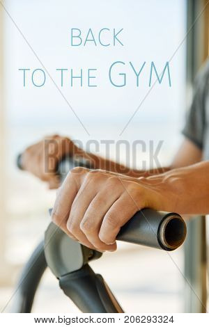 closeup of a young caucasian man in a gray t-shirt using an elliptical trainer and the text back to the gym