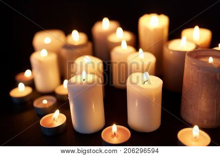 mourning and commemoration concept - candles burning in darkness over black background