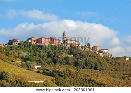 Small town of Diano D'Alba and autumnal vineyards on the hill under blue sky in Piedmont, Northern Italy.