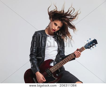 cool headbanging rock and roll woman playing electric guitar on grey studio background