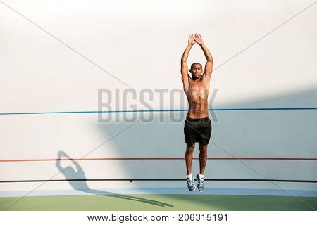 Full length portrait of a half naked african fitness man jumping at the track field outdoors