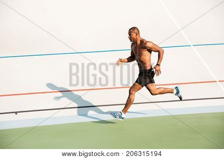 Full length portrait of a strong half naked sportsman running on a track field outdoors