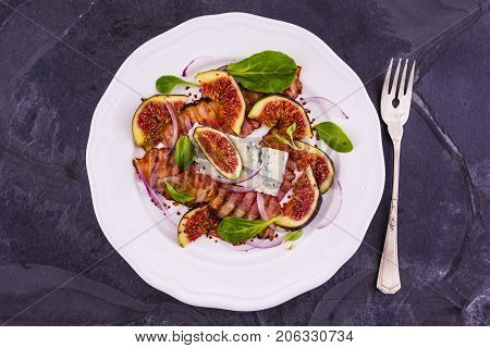Figs and fried bacon with small lettuce leaves served on a white plate. Italian food.