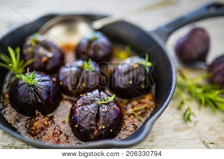 Oven-baked figs with herbs and honey on frying pan with spoon. Italian food.