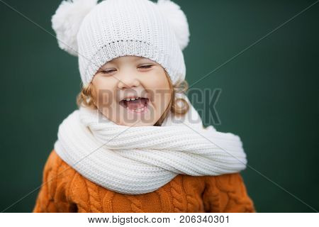 Adorable happy little girl wearing white knitted hat and scarf autumn day
