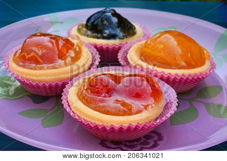 Punnets of dough filled in with various candied fruits served in pink glass plate close up side view