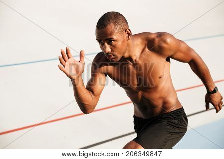 Portrait of a half naked muscular sportsman running on a track field outdoors