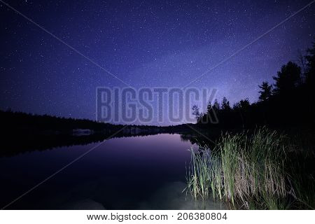 Lake at night with amazing starry sky and reflections in the water. Natural outddors travel dark background.
