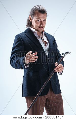 The mature bearded man in a suit holding cane. Isolated on a blue studio background.
