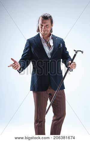 The mature bearded man in a suit holding cane. Isolated on a blue studio background.