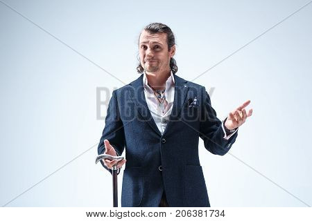 The mature bearded man in a suit holding cane. Isolated on a blue studio background.