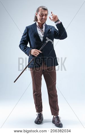 The mature bearded man in a suit holding cane. Isolated on a blue studio background.