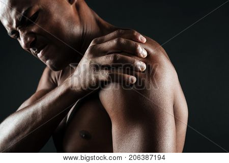 Cropped photo of young shirtless afro american man with shoulder pain, isolated on black background
