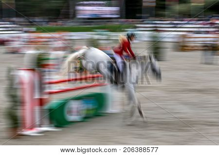 Abstract image with a moving rider and horse at show jumping on blurred background.