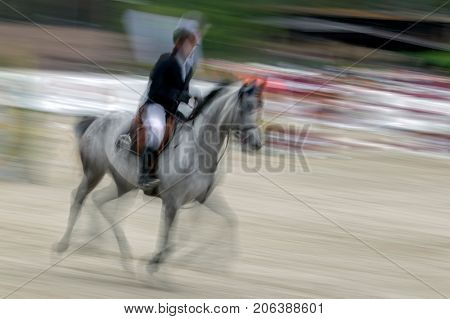 Abstract image with a moving rider and horse at show jumping on blurred background.