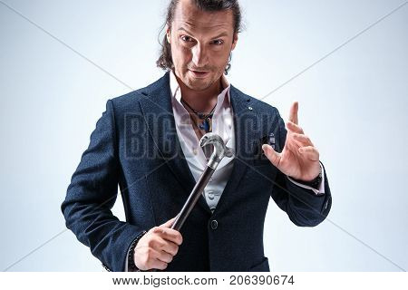 The mature bearded man in a suit holding cane. Isolated on a blue studio background.