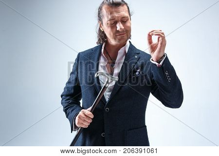 The mature bearded man in a suit holding cane. Isolated on a blue studio background.