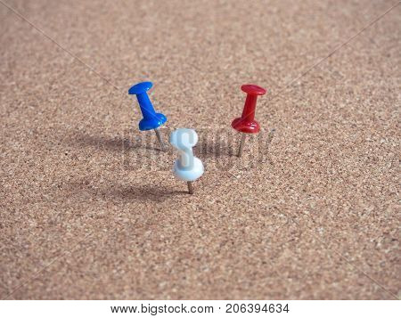 Blue white and red pins on brown cork board.