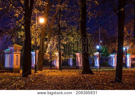Night autumn view of illuminated alley and fence in Nikolskiy garden St. Petersburg Russia