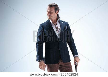 The mature bearded man in a suit holding cane. Isolated on a blue studio background.