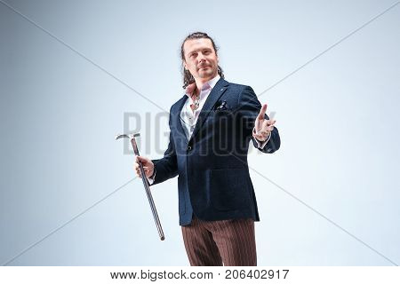 The mature bearded man in a suit holding cane. Isolated on a blue studio background.