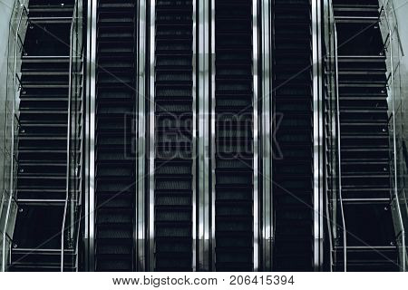 Top view of contemporary glass and chrome escalator line of four tracks with two stairways on both sides in airport terminal deport or modern mall building strong metallic specular