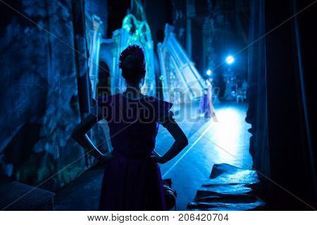ballet, dancing, magic concept. in ghostly blue light tender silhouette of slender ballerina wearing pink dress with short sleeves waiting for her turn backstage