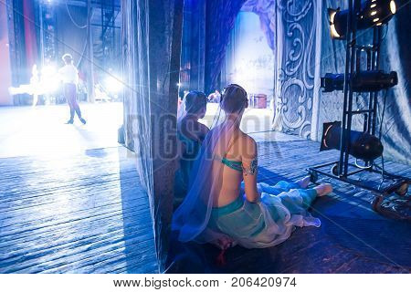 ballet, illumination, backstage concept. in the light of spotlights adorable ballerinas wearing turquoise costumes of east beauties sitting on little pillows and waiting in the wings for their cue