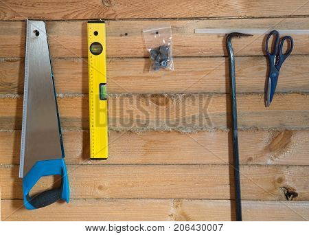 Tools for building on wooden background of pine forest. Bright yellow level saw scissors hanging on the wall on the screws. Between the pine rail laid with linen tape.