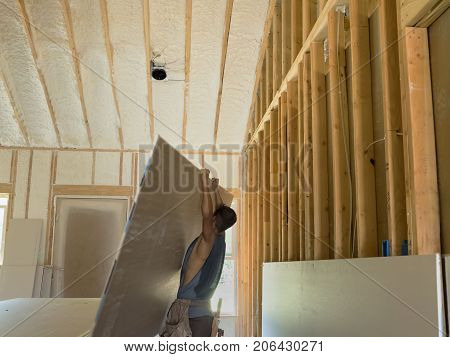 Sheetrocker on construction site is pulling up sheetrock to attach to the wacll