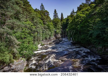 Summer view of a rushing stream, forest and small cottage in Invermoriston in the Scottish Highlands.
