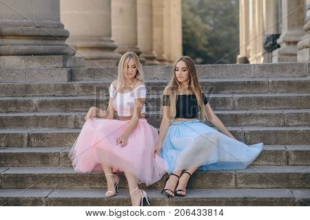 Two beautiful girls in colored skirts sit on stairs