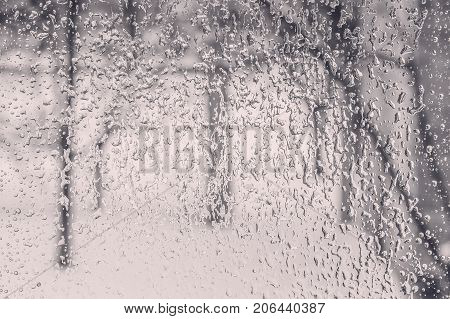 Texture of the ice and drops on the window glass in a bad winter day close up. Photo black and white toned